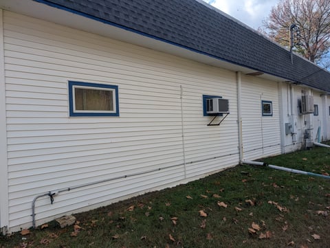White vinyl siding mobile home with dark roof, window, and air conditioning unit on grass lot