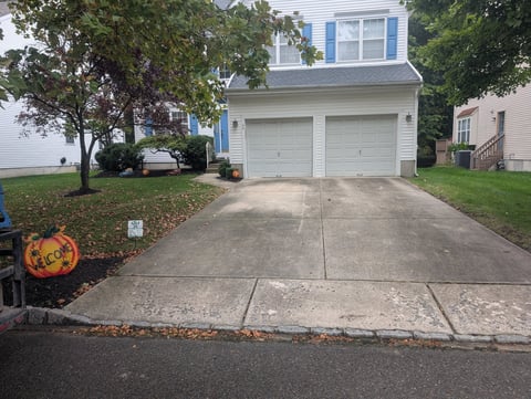 Two-car garage driveway with white garage doors, surrounded by green lawn and trees, on a residential street