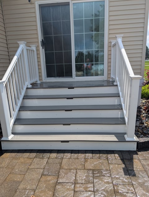 Gray and white composite deck with white railings leading to sliding glass doors on a house with stone patio below
