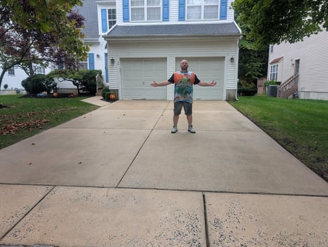 Man standing on driveway with arms outstretched in front of two-car garage of blue and white house