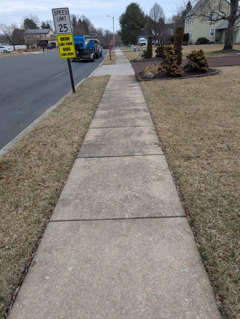 Concrete sidewalk extending down a residential street with a 25 mph speed limit sign visible in the foreground